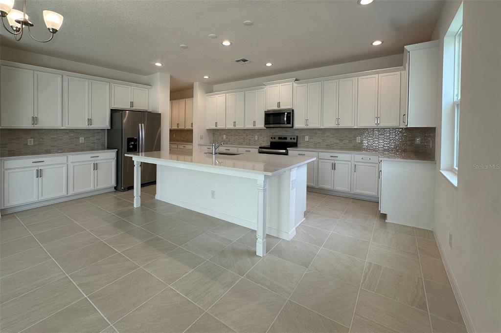 A bright kitchen features white cabinetry, a central island, stainless steel appliances, and tile flooring — 761 FARFIELDS STREET, DELAND, FL