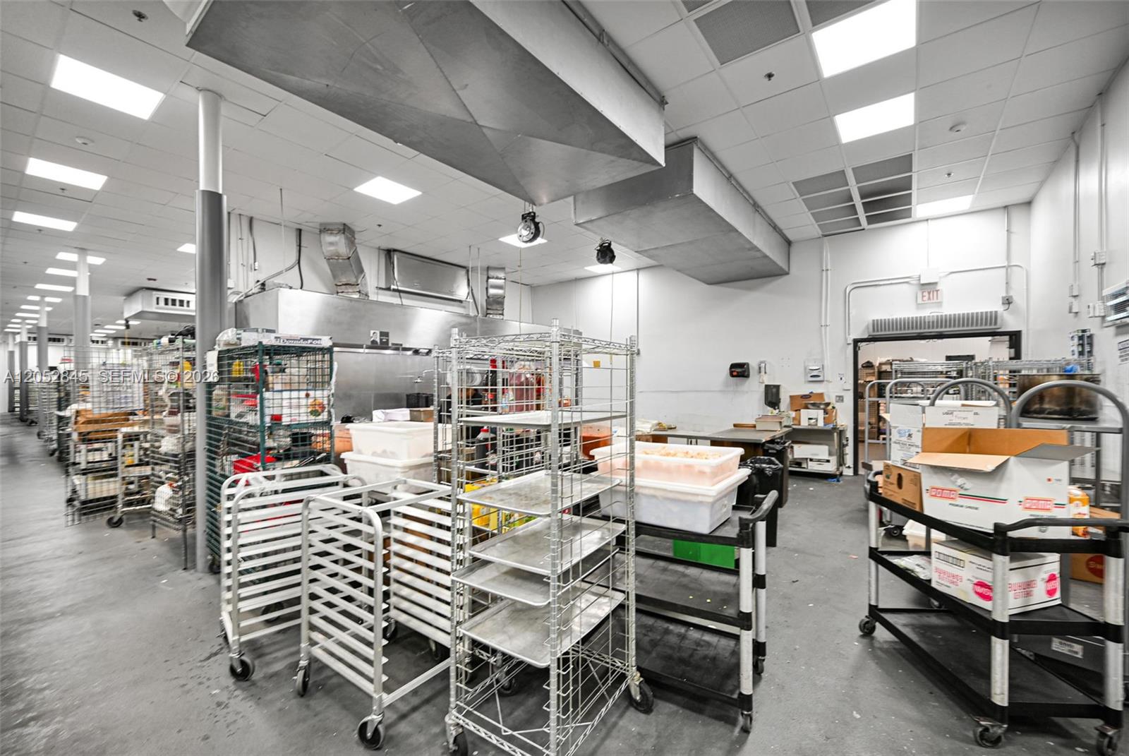 A commercial kitchen features metal shelving units, rolling carts, and stainless steel ventilation hoods — 1395 E 11th Ave, Hialeah FL 33010, HIALEAH, FL