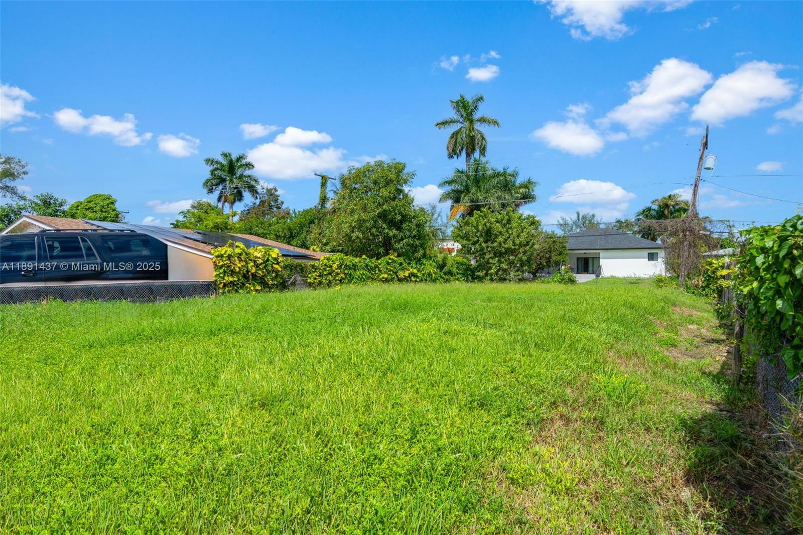 A large, grassy vacant lot is bordered by a fence, trees, and neighboring houses — 1453 NE 117th St, Miami FL 33161, MIAMI, FL