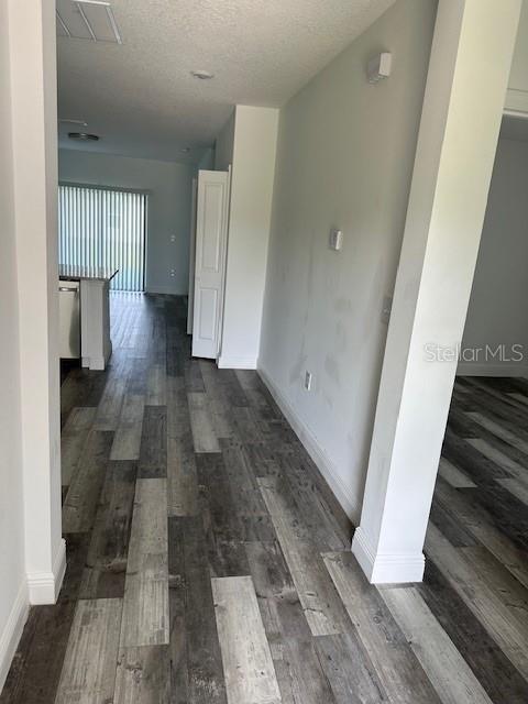 A hallway with wood-look flooring leads toward a kitchen area with sliding glass doors — 542 KILIMANJARO, KISSIMMEE, FL