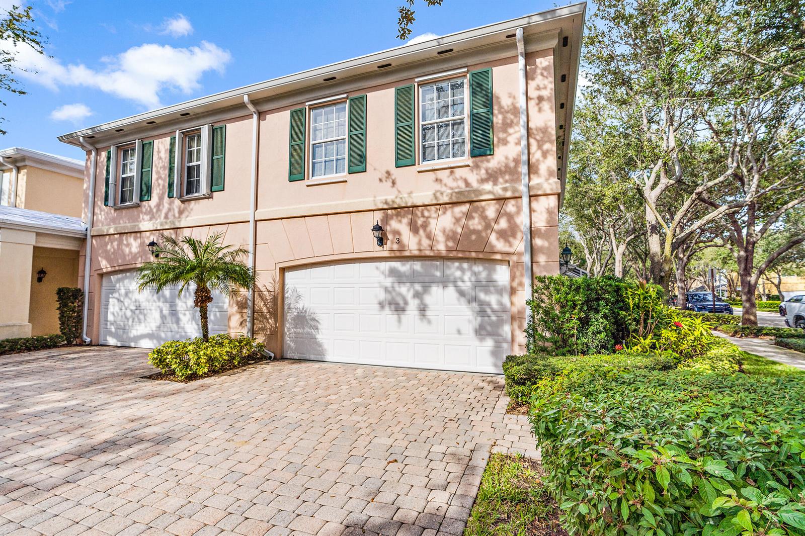 A two-story peach-colored townhouse features a double garage, green shutters, and a paved driveway — 3 Oakland Court, Tequesta FL 33469, TEQUESTA, FL