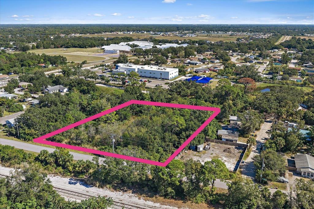 An aerial view shows a rectangular, tree-covered vacant lot outlined in pink near a road — LEONARD REID AVENUE, SARASOTA, FL
