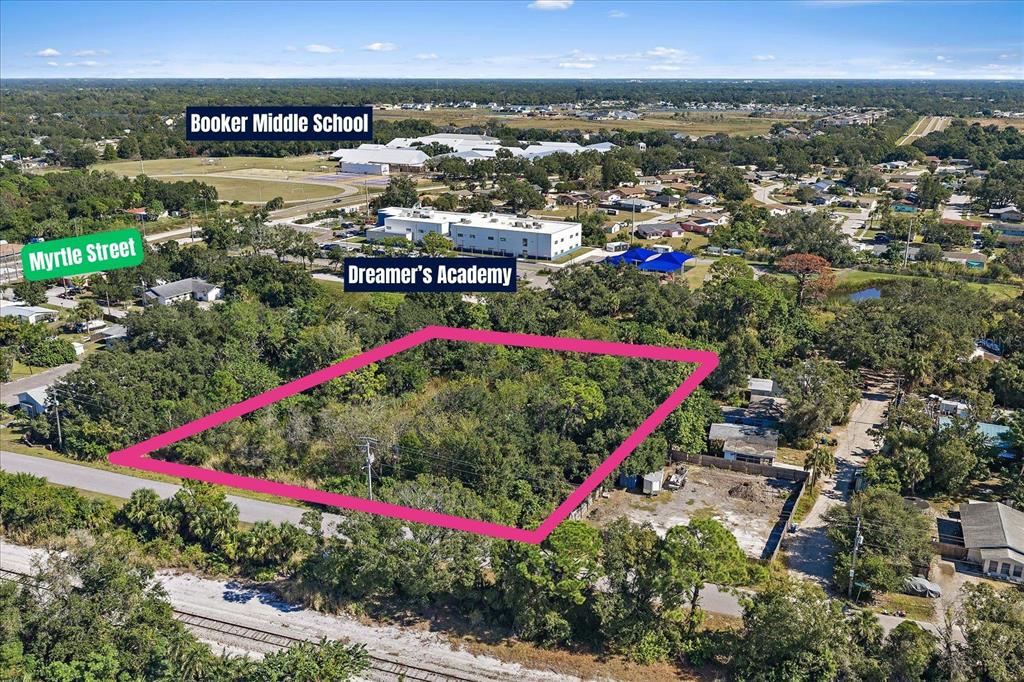 An aerial view shows a vacant, tree-covered lot outlined in pink near schools and streets — LEONARD REID AVENUE, SARASOTA, FL