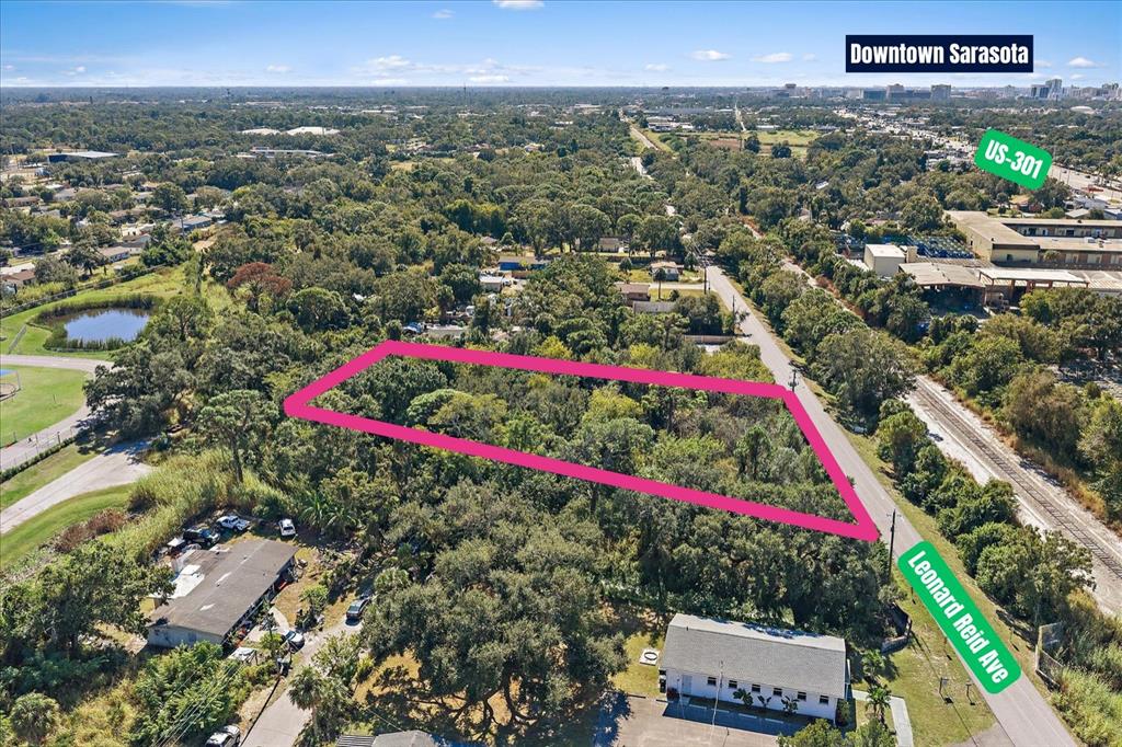 An aerial view shows a rectangular, tree-covered vacant lot outlined in pink along a road — LEONARD REID AVENUE, SARASOTA, FL