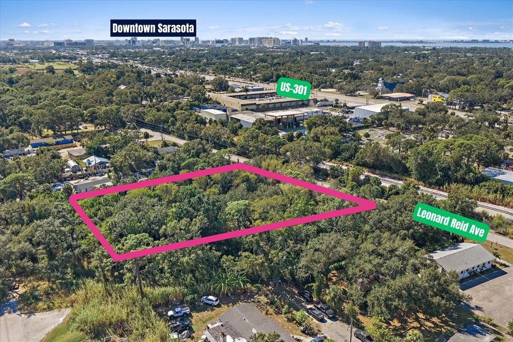 An aerial view shows a rectangular, tree-covered vacant lot outlined in pink near a road — LEONARD REID AVENUE, SARASOTA, FL
