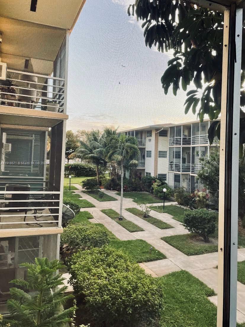 A view from a balcony overlooking a courtyard with walkways, palm trees, and apartment buildings — 1355 NE 167th St # 209, Miami FL 33162, MIAMI, FL