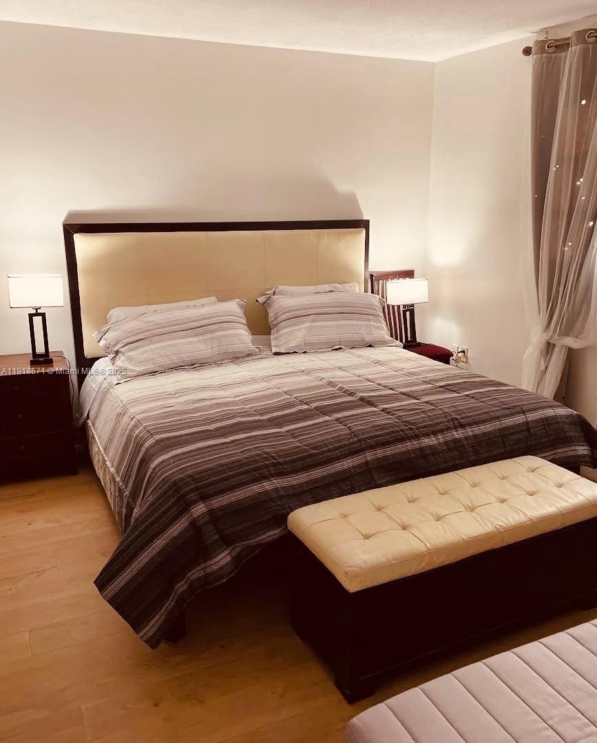A bedroom features a bed with a striped comforter, a tufted bench, and two lamps — 1355 NE 167th St # 209, Miami FL 33162, MIAMI, FL