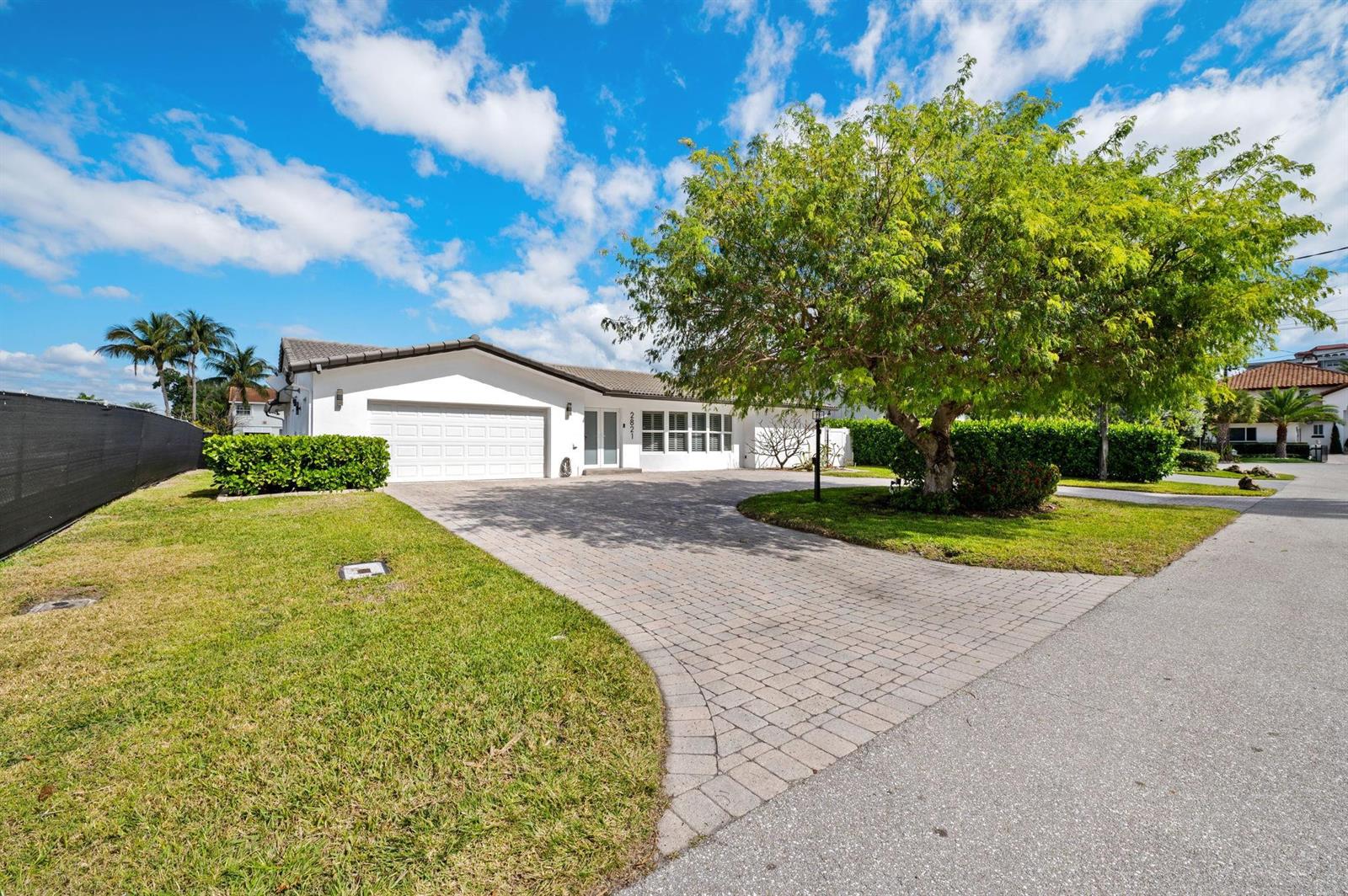A single-story white house features a paved driveway, a large tree, and a green hedge — 2821 NE 9th Court, Pompano Beach FL 33062, POMPANO BEACH, FL