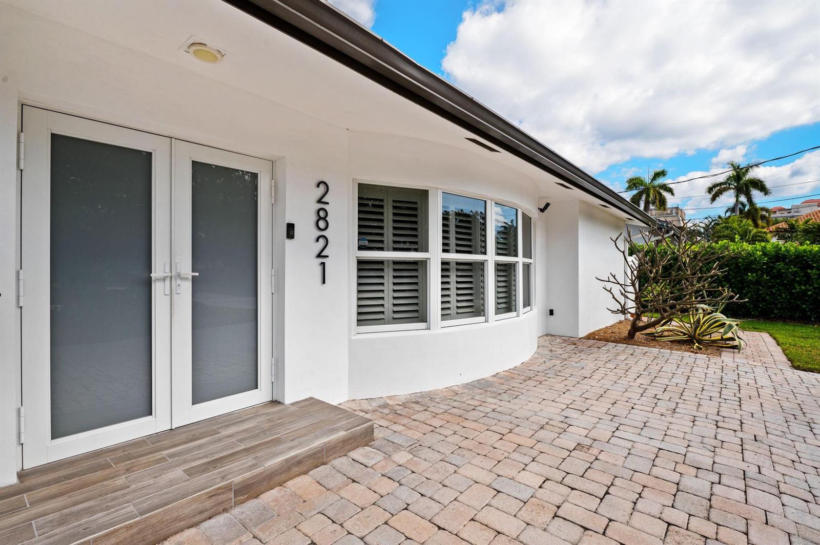 A white house exterior features a curved wall, double glass doors, and a paver patio — 2821 NE 9th Court, Pompano Beach FL 33062, POMPANO BEACH, FL