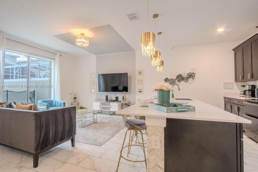 A modern open-concept kitchen and living area features white marble floors and dark cabinetry — 962 splash Shot  Pl, Kissimmee FL 33896, KISSIMMEE, FL