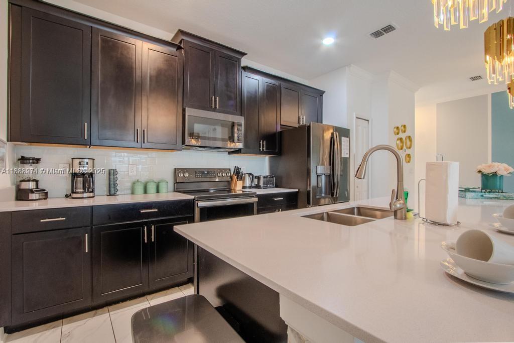A kitchen features dark wood cabinets, white countertops, stainless steel appliances, and a central island — 962 splash Shot  Pl, Kissimmee FL 33896, KISSIMMEE, FL
