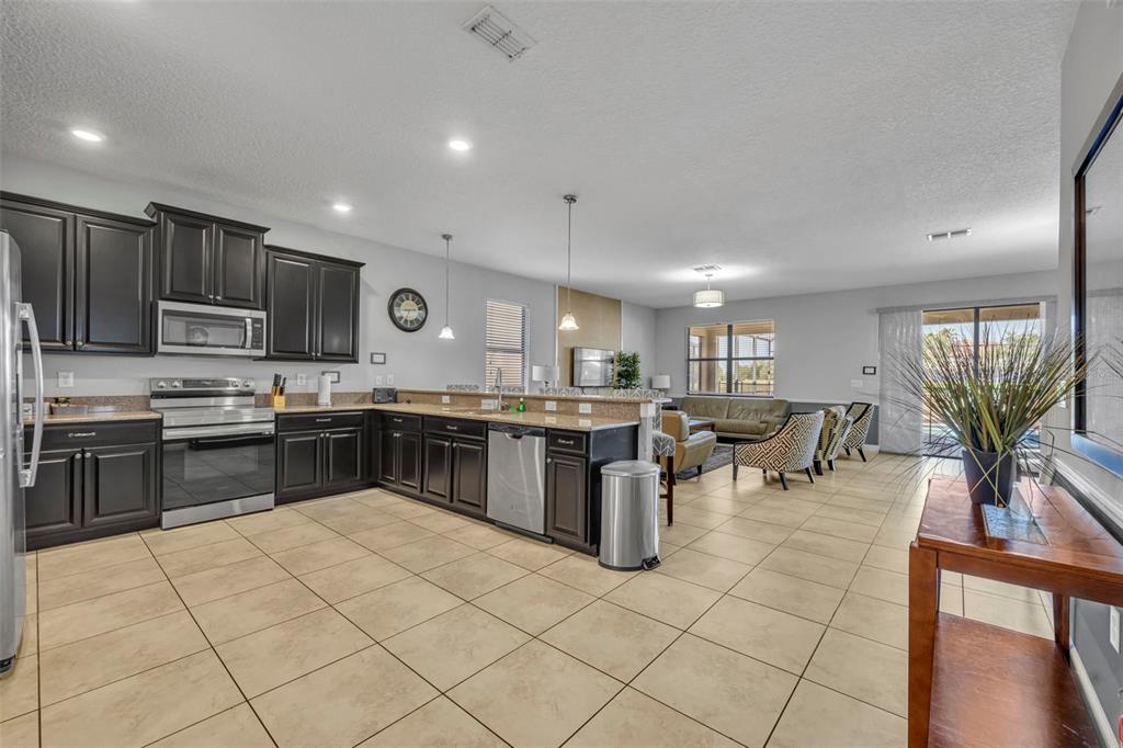 A kitchen with dark cabinets and stainless steel appliances opens to a living area — 1435 ROLLING FAIRWAY DRIVE, DAVENPORT, FL