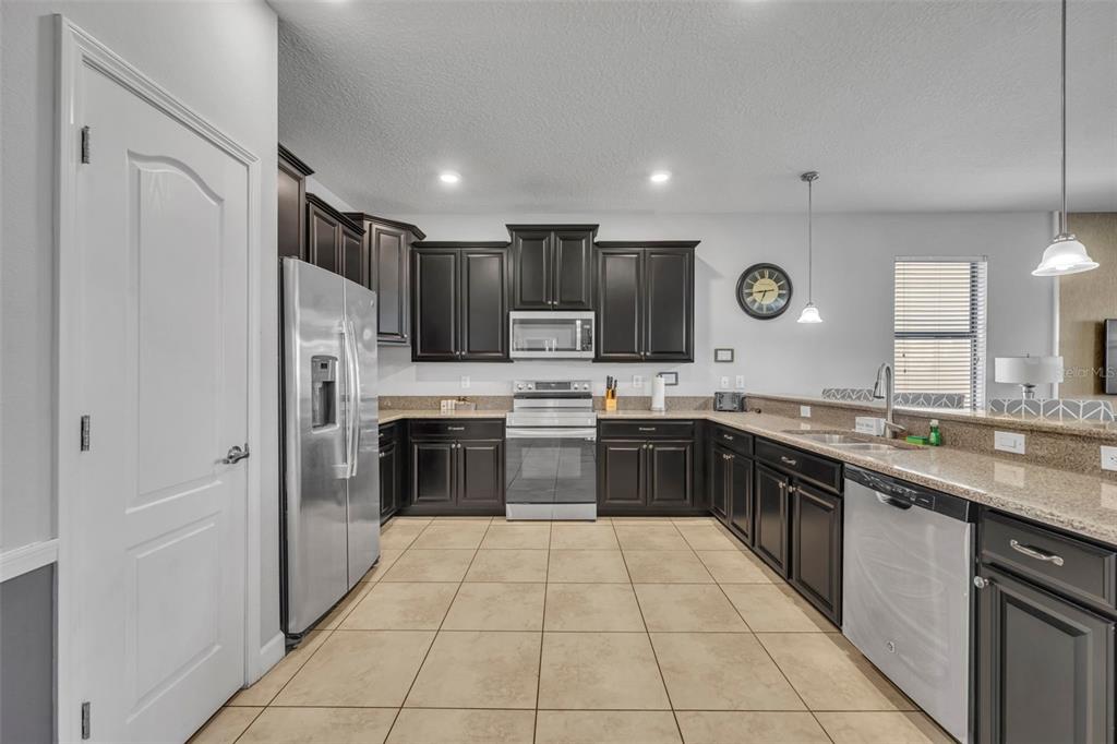 A kitchen features dark wood cabinets, stainless steel appliances, and tan tile flooring — 1435 ROLLING FAIRWAY DRIVE, DAVENPORT, FL