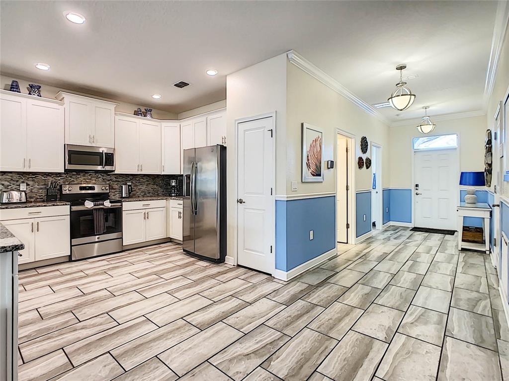 A kitchen with white cabinets, stainless steel appliances, and blue wainscoting leads to an entryway — 9095 HAZARD STREET, DAVENPORT, FL