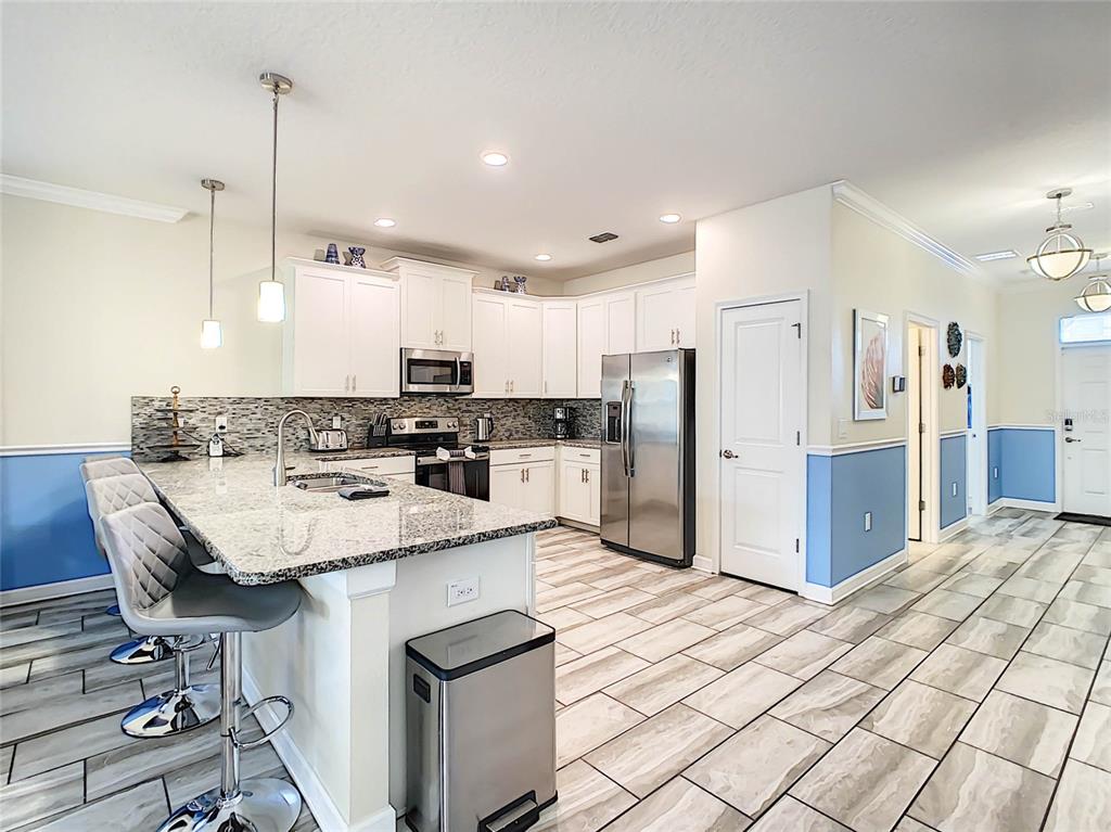 A kitchen features white cabinets, granite countertops, stainless steel appliances, and light-colored tile flooring — 9095 HAZARD STREET, DAVENPORT, FL