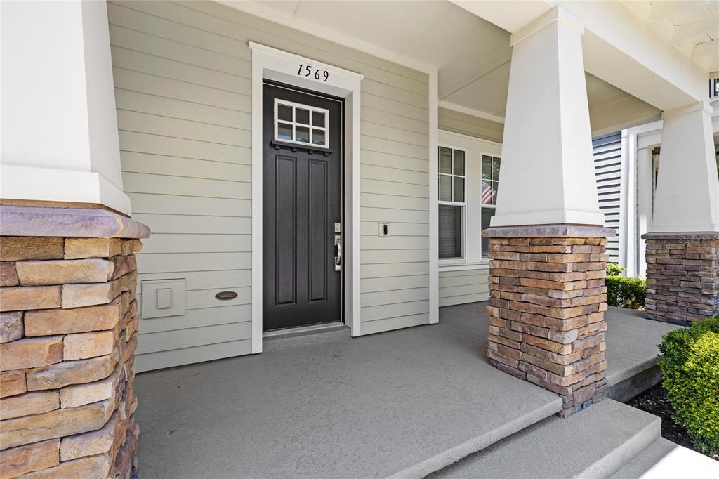A covered front porch features a black door, stone-based columns, and light-colored horizontal siding — 1569 RESOLUTE STREET, KISSIMMEE, FL