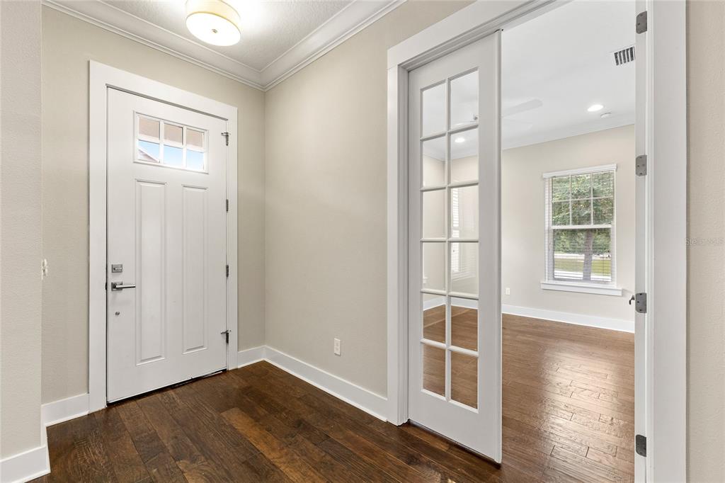 An entryway with dark wood flooring, a white front door, and glass-paned French doors — 1569 RESOLUTE STREET, KISSIMMEE, FL