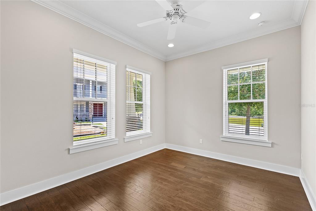An empty room with hardwood floors, a ceiling fan, and three windows overlooking the exterior — 1569 RESOLUTE STREET, KISSIMMEE, FL