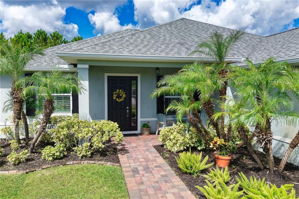 A front view of a house with a brick walkway, palm trees, and a black door — SEBASTIAN, FL