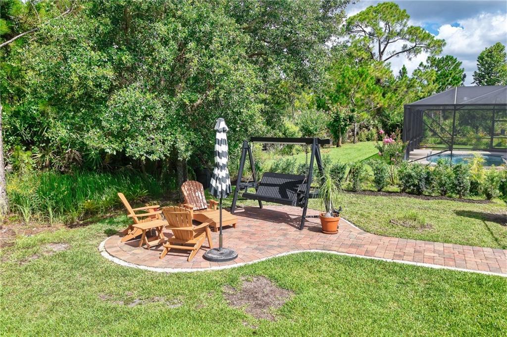 A brick patio features wooden Adirondack chairs, a black porch swing, and a striped umbrella — SEBASTIAN, FL