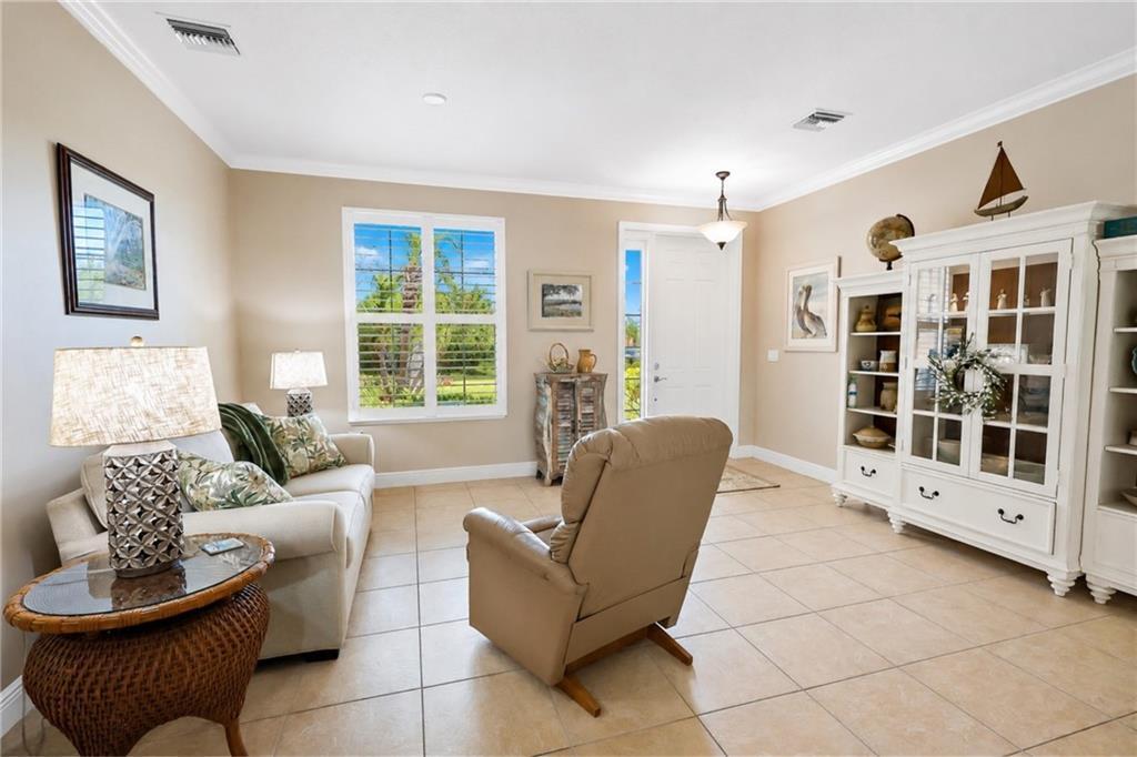 A living room features beige walls, tile flooring, a sofa, a recliner, and a white cabinet — SEBASTIAN, FL