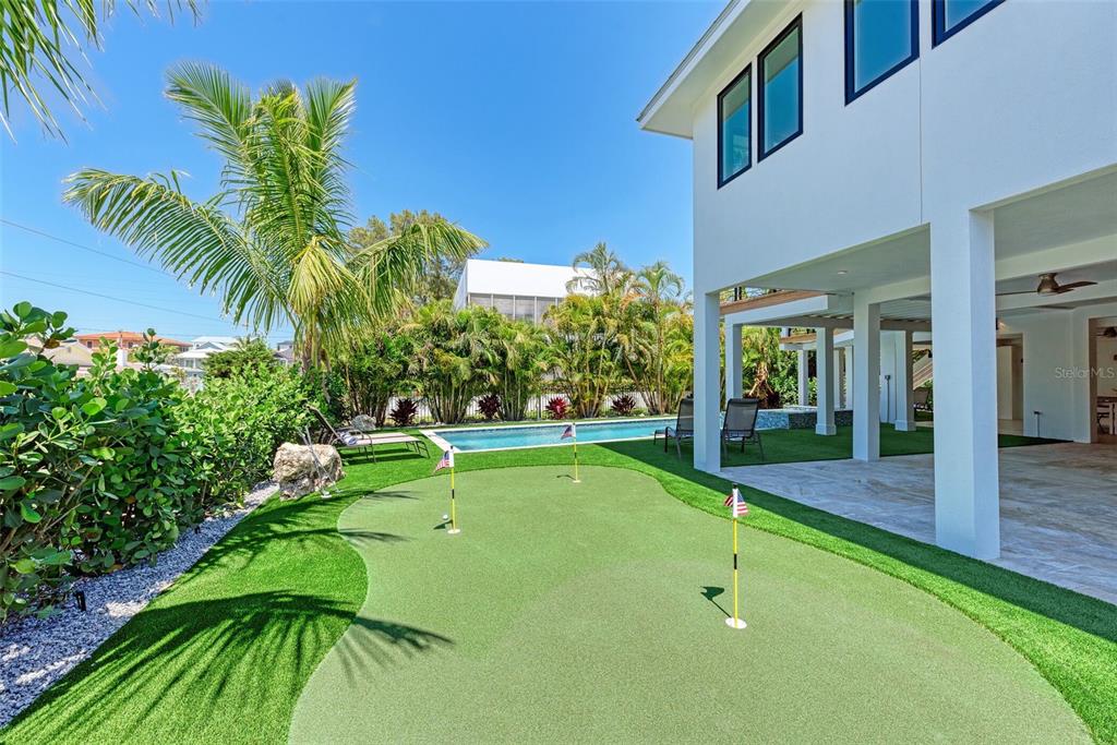 A backyard putting green sits beside a swimming pool and a modern white house — 256 GLADIOLUS STREET, ANNA MARIA, FL