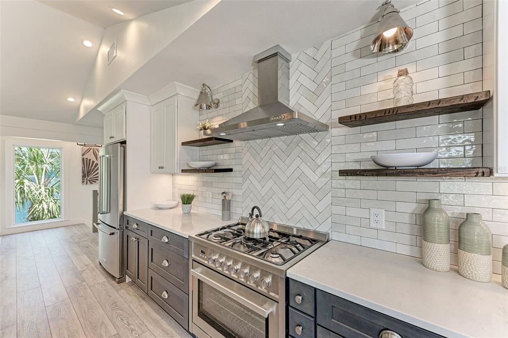 A kitchen features dark lower cabinets, white upper cabinets, a herringbone backsplash, and floating shelves — 256 GLADIOLUS STREET, ANNA MARIA, FL
