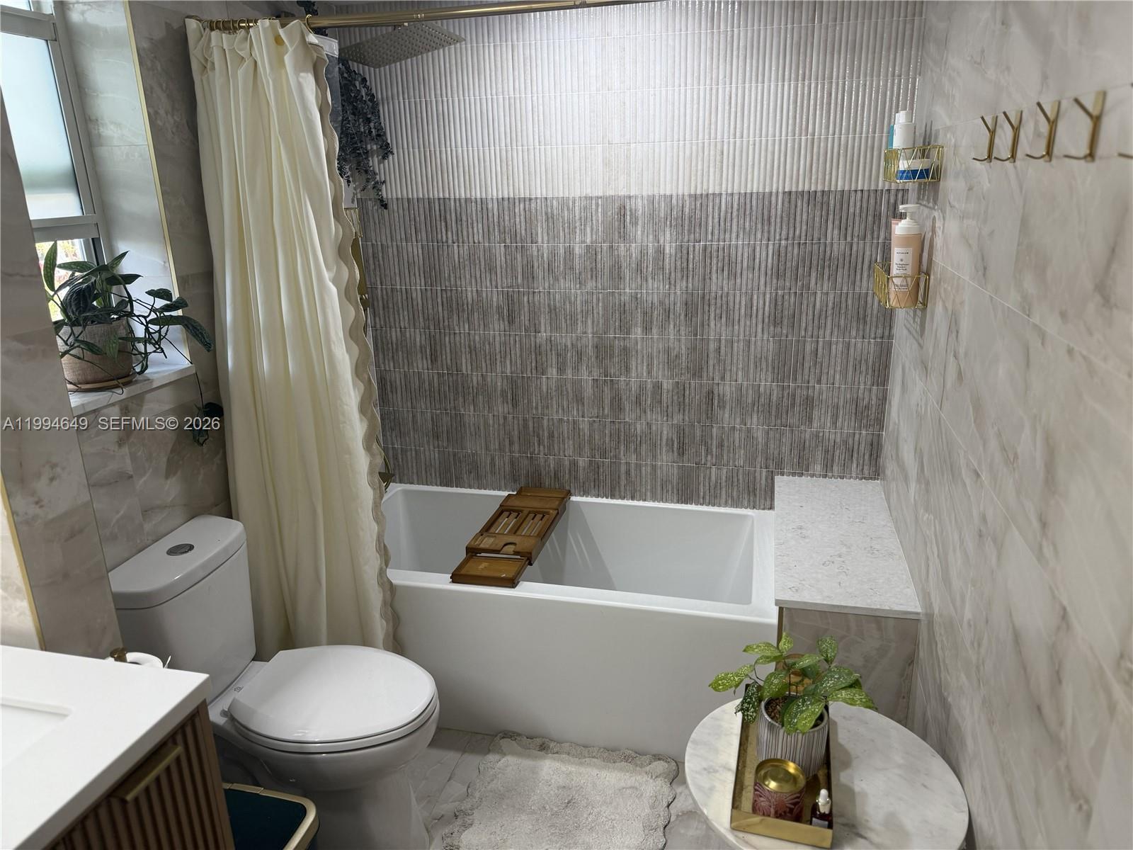 A bathroom features a white bathtub, a toilet, a vanity, and textured wall tiles — 1519 Drexel Ave # 200, Miami Beach FL 33139, MIAMI BEACH, FL