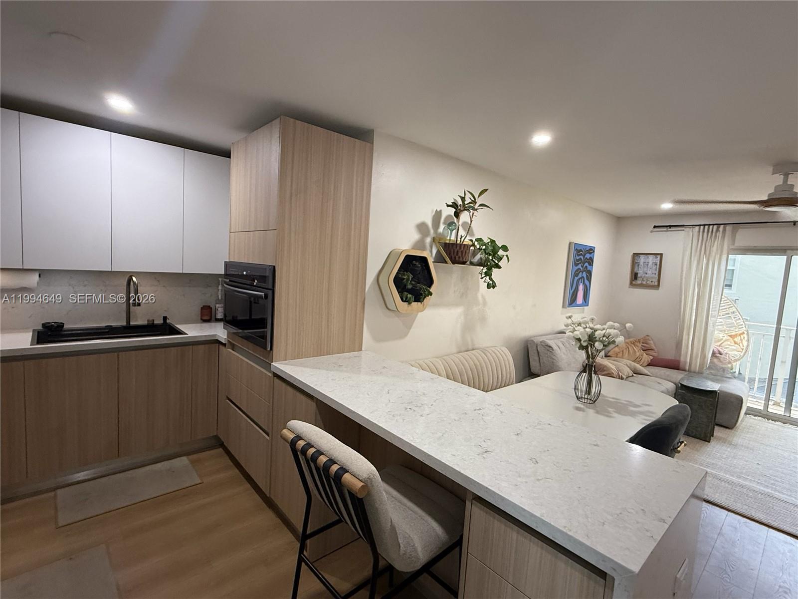 A modern kitchen features light wood cabinetry, white countertops, and an attached dining nook — 1519 Drexel Ave # 200, Miami Beach FL 33139, MIAMI BEACH, FL