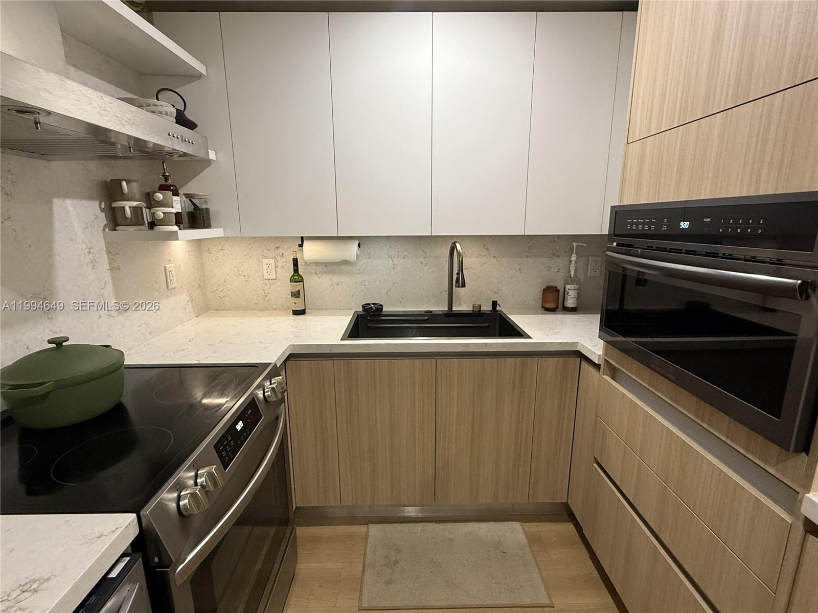 A modern kitchen features light wood cabinetry, white upper cabinets, and a black sink — 1519 Drexel Ave # 200, Miami Beach FL 33139, MIAMI BEACH, FL