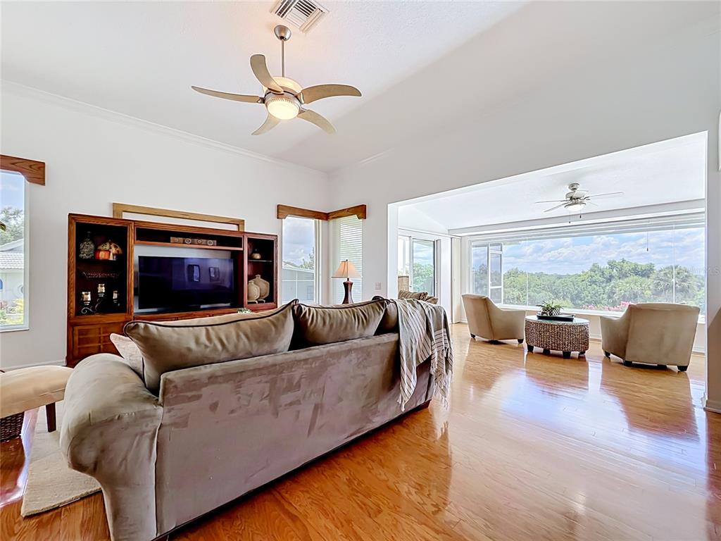 A living room features a large sofa, wooden entertainment center, and a sunroom with views — 6042 TOPSAIL ROAD, LADY LAKE, FL