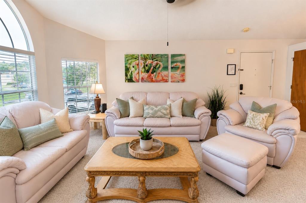 A living room features light-colored sofas, a wooden coffee table, and flamingo wall art — 2440 SWEETWATER CLUB CIRCLE UNIT 40, KISSIMMEE, FL