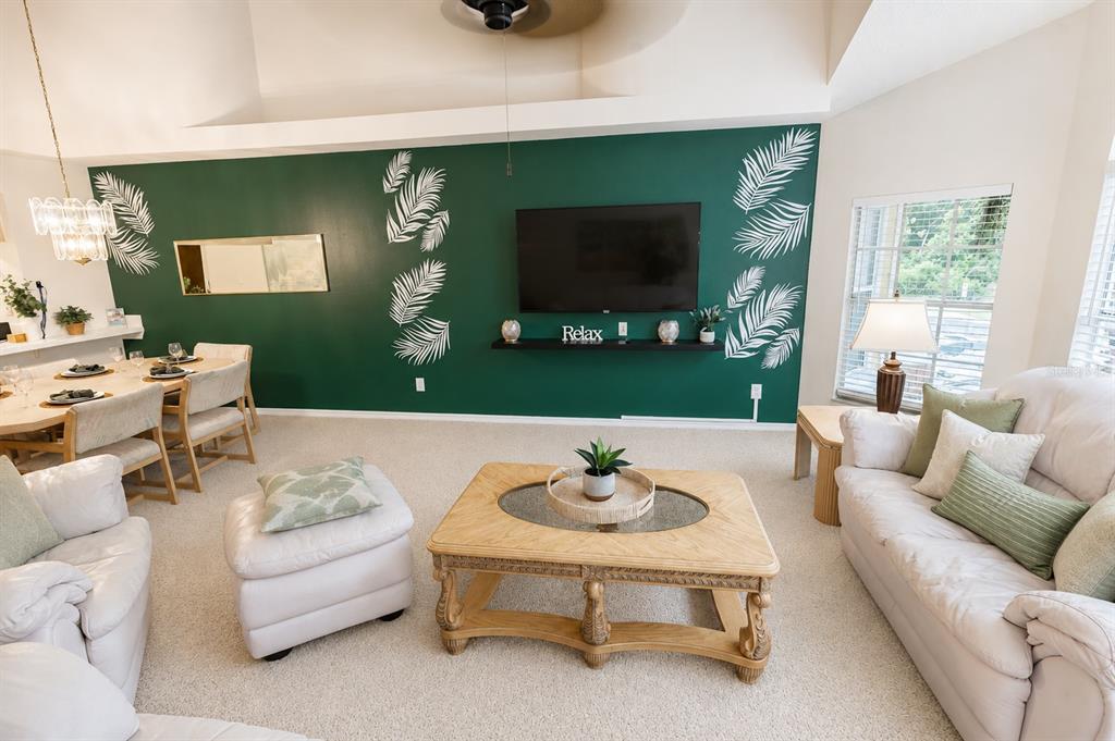 A living room with a green accent wall, television, and light-colored furniture on carpeted floors — 2440 SWEETWATER CLUB CIRCLE UNIT 40, KISSIMMEE, FL