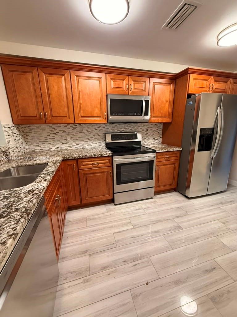 A kitchen features wood cabinets, stainless steel appliances, granite countertops, and light-colored wood-look flooring — 4182 S Pine Island Rd, Davie FL 33328, DAVIE, FL