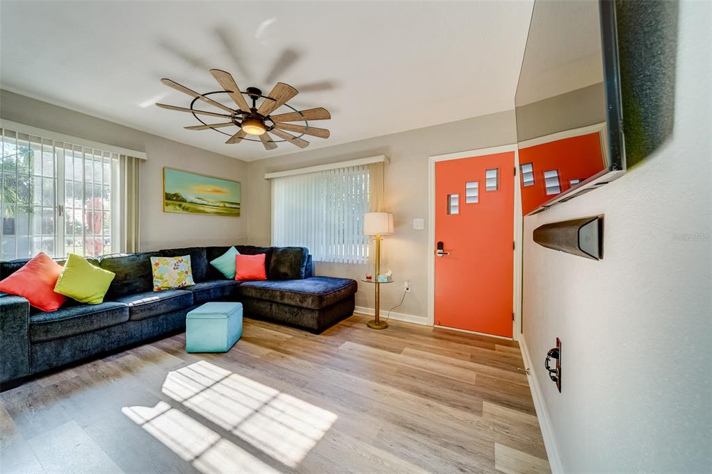 A living room features a dark sectional sofa, wood-look flooring, and a bright orange door — 10802 MOHAWK ROAD, ST PETERSBURG, FL
