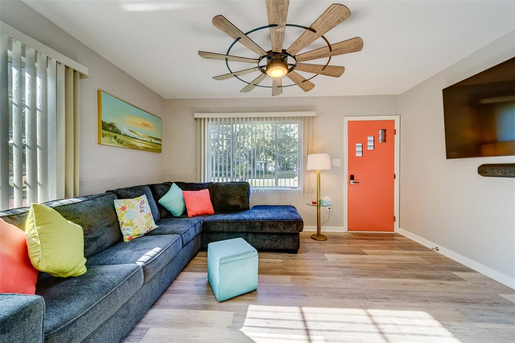 A living room features a dark sectional sofa, a coral door, and a ceiling fan — 10802 MOHAWK ROAD, ST PETERSBURG, FL