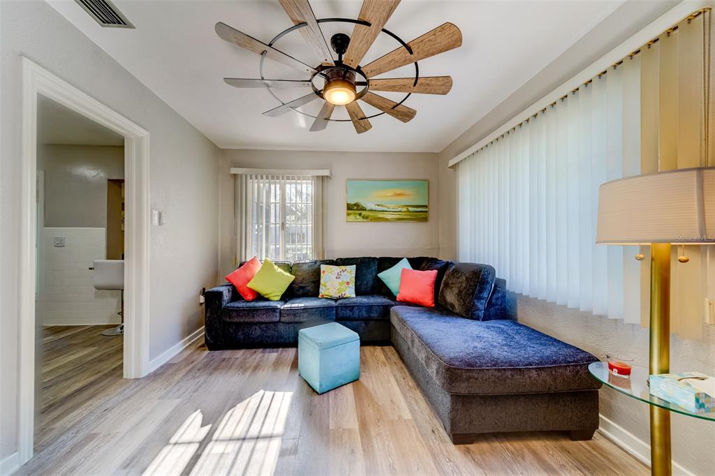A living room features a dark sectional sofa, wood-look flooring, and a unique ceiling fan — 10802 MOHAWK ROAD, ST PETERSBURG, FL