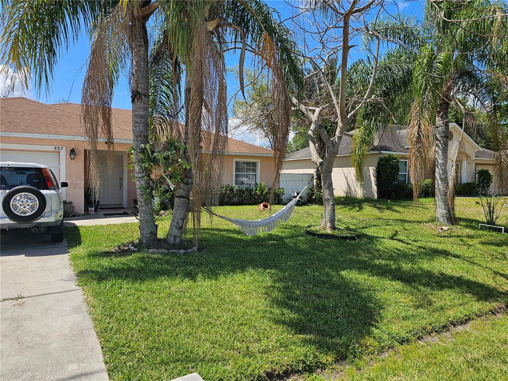 A front view of a single-story house with a hammock hanging between two palm trees — 557 EAGLE COURT, KISSIMMEE, FL