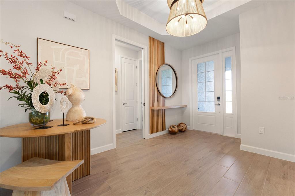 A bright entryway features light wood flooring, a decorative wood slat wall, and a round mirror — 19804 TROUT TERRACE, LAKEWOOD RANCH, FL