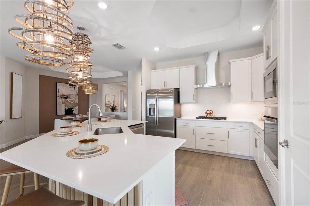 A modern kitchen features white cabinetry, a large quartz island, and stainless steel appliances — 19804 TROUT TERRACE, LAKEWOOD RANCH, FL
