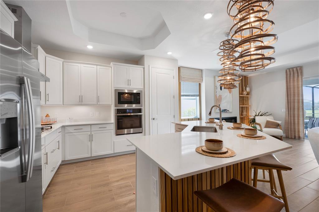 A modern kitchen features white cabinetry, a large island with wood paneling, and pendant lighting — 19804 TROUT TERRACE, LAKEWOOD RANCH, FL