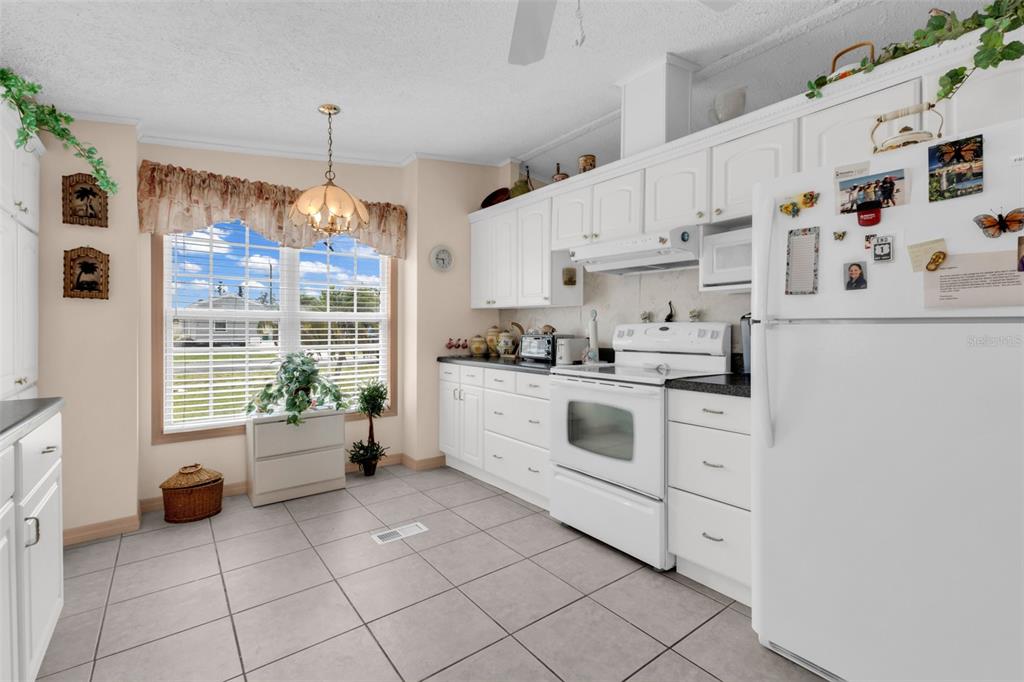 A kitchen features white cabinetry, a white stove, a refrigerator, and light-colored tile flooring — 29180 CRAWFORD AVENUE, PUNTA GORDA, FL