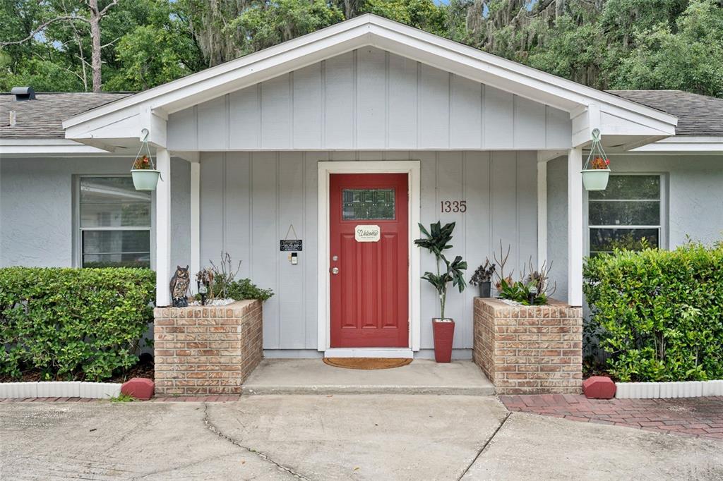 The exterior of a house features a red front door, brick planters, and a covered porch — 1335 YVONNE STREET, APOPKA, FL