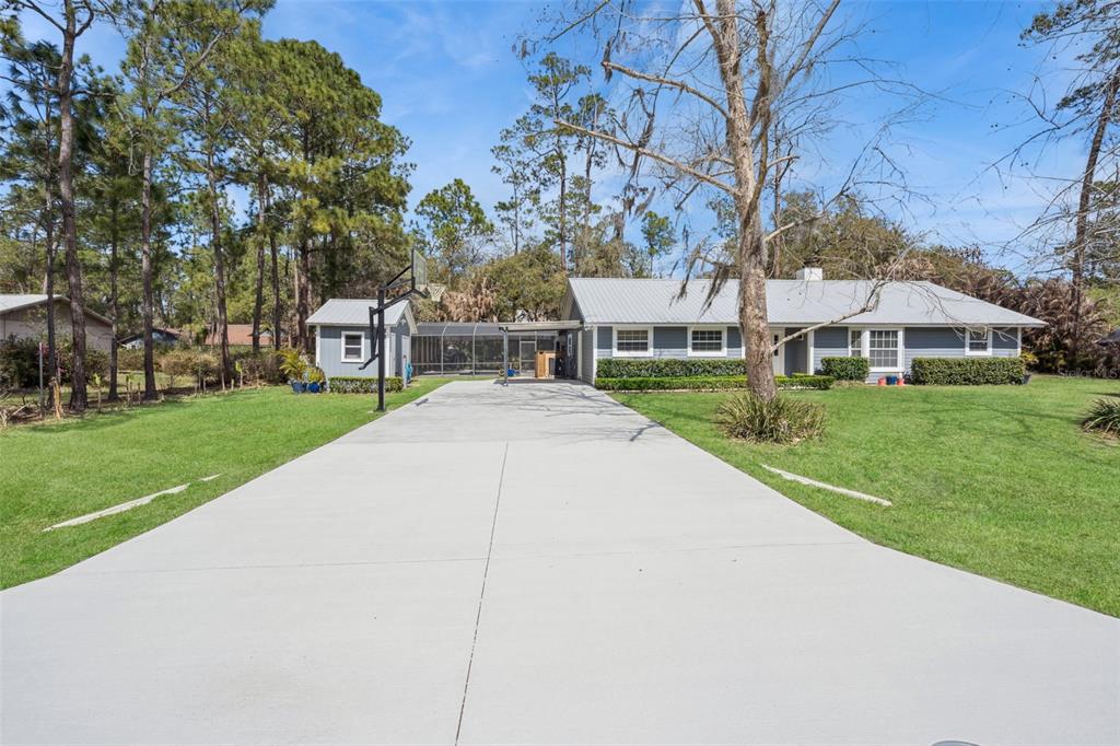 A single-story house with a grey exterior, metal roof, and a large concrete driveway — 14335 FRESNO DRIVE, ORLANDO, FL