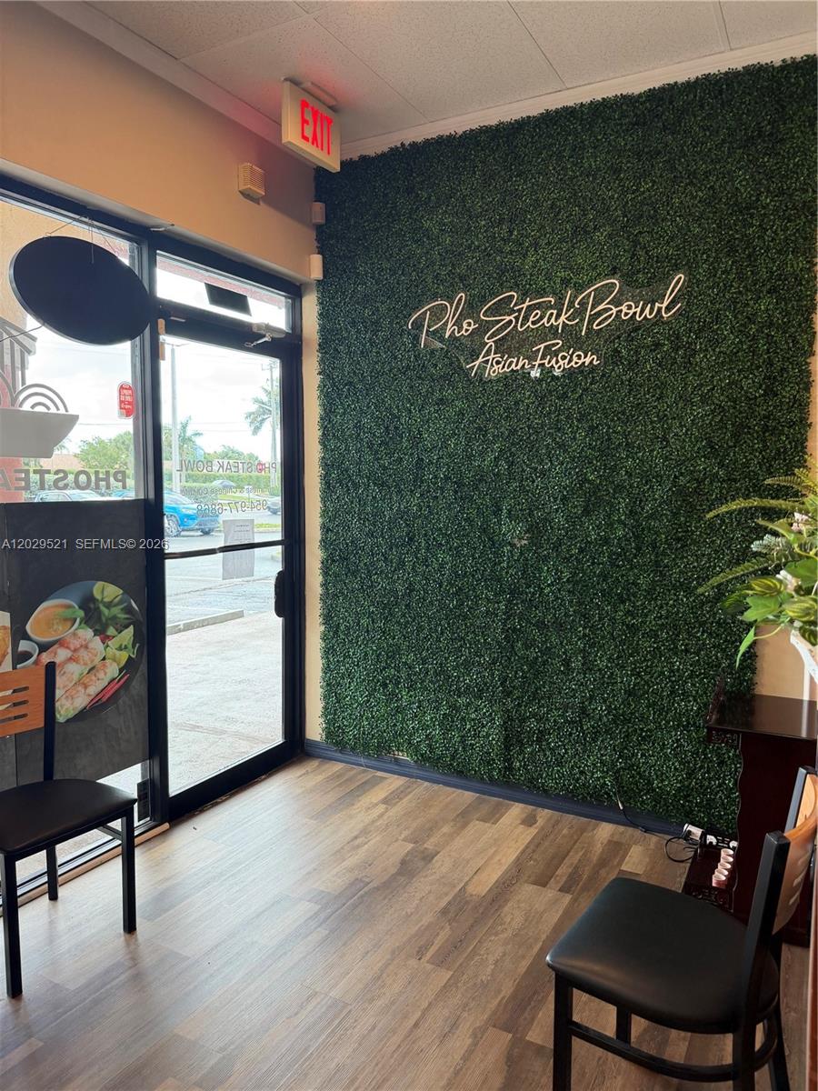 A restaurant entrance features a green faux-foliage wall with neon signage and wood-look flooring — 7462 Royal Palm Blvd, Margate FL 33063, MARGATE, FL