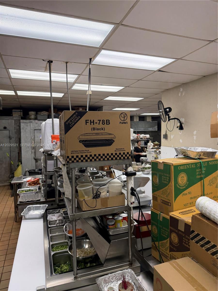 A commercial kitchen features stainless steel prep stations, stacked boxes of food containers, and overhead lighting — 7462 Royal Palm Blvd, Margate FL 33063, MARGATE, FL