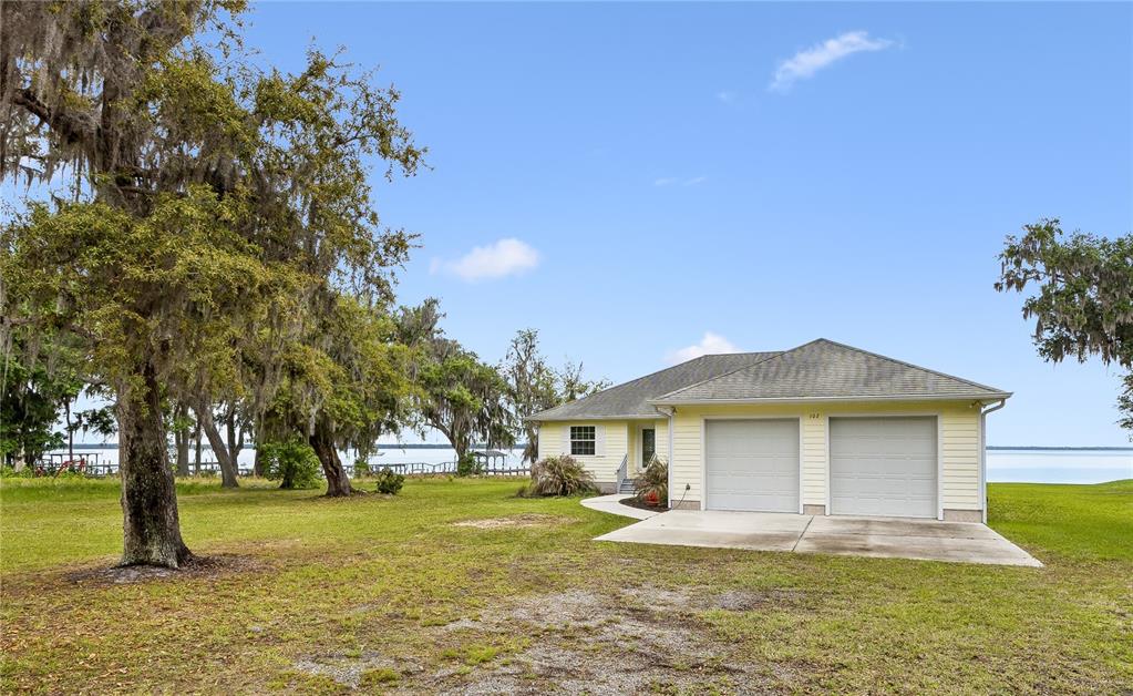 A light yellow house with a two-car garage sits on a grassy waterfront lot — 102 SANDRA LANE, CRESCENT CITY, FL