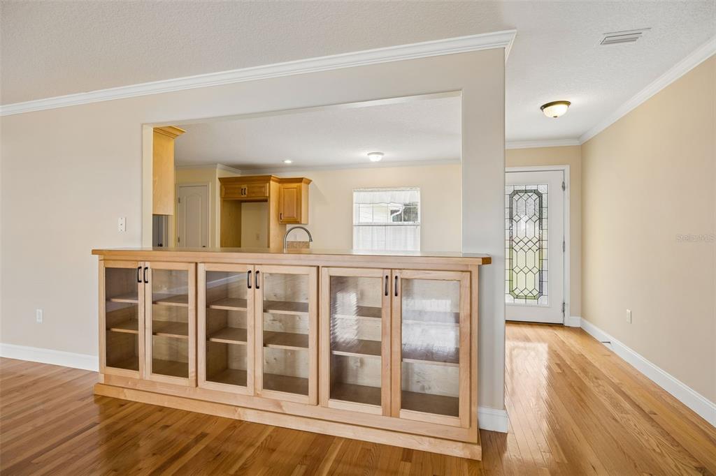 A kitchen pass-through features light wood cabinetry with glass doors and hardwood flooring — 102 SANDRA LANE, CRESCENT CITY, FL
