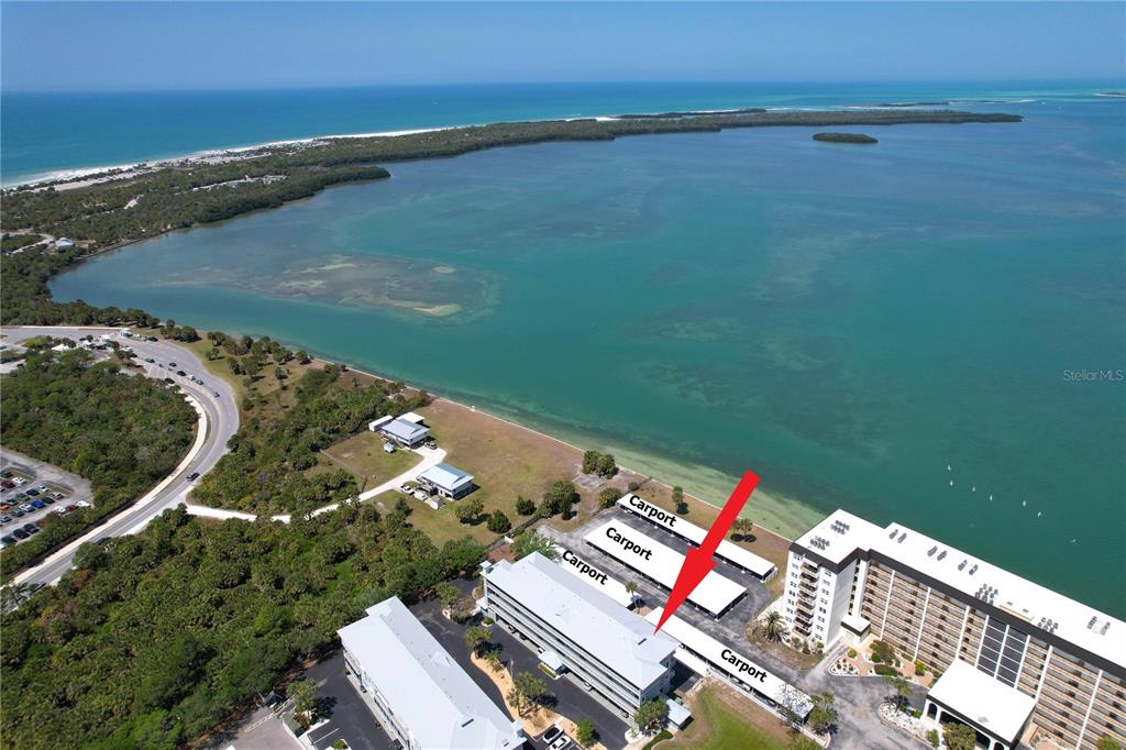 An aerial view shows a coastal apartment complex with carports near a large bay — 7 ISLAND PARK PLACE UNIT 204, DUNEDIN, FL