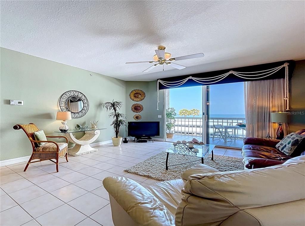 A living room features tile floors, a ceiling fan, and a balcony overlooking the ocean — 7 ISLAND PARK PLACE UNIT 204, DUNEDIN, FL